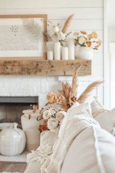 a living room filled with white furniture and flowers on the fireplace mantel above it