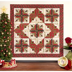 a christmas quilt hanging on the wall next to a small tree and presents under it