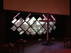 a cross in the middle of a stage with lights on and buildings projected behind it