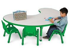 a little boy sitting at a table with a book in front of him and some chairs around it