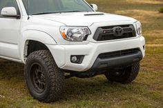 a white toyota truck parked on top of a grass covered field with trees in the background