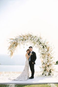 a bride and groom standing under an arch with flowers