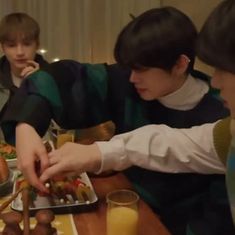 three boys sitting at a table with food in front of them and one boy reaching for something