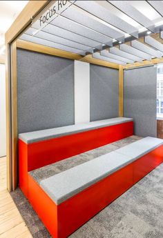 an office cubicle with red and grey benches in front of the wall, on top of carpeted flooring