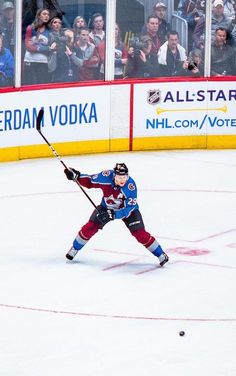 an ice hockey player is about to make contact with the puck while fans look on