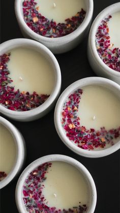 four white bowls filled with liquid and sprinkles on top of a table