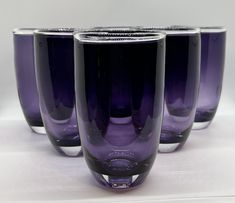 four purple glass cups sitting on top of a white table