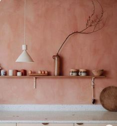 a kitchen with pink walls and white counter tops, including an overhead shelf filled with pots and pans