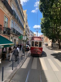 a red trolley car traveling down a street next to tall buildings and people walking on the sidewalk