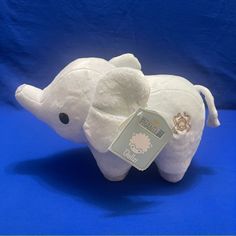 a white stuffed elephant with a tag on it's ear and ears, sitting against a blue background