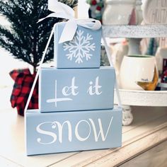 three wooden blocks that say let it snow on top of each other in front of a christmas tree