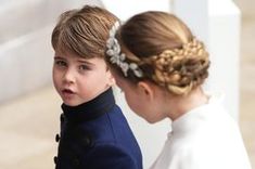 the young boy is wearing a blue coat and standing next to an older woman in a white dress