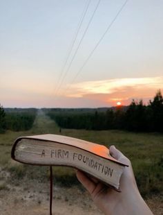 a hand holding an open book with writing on it in the middle of a field