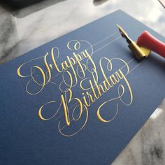 a blue birthday card with gold lettering on it and a fountain pen next to it