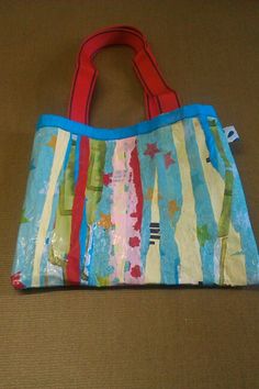 a handbag sitting on top of a brown floor next to a red bag with blue handles