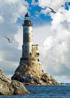 a large light house sitting on top of a rocky cliff next to the ocean under a cloudy blue sky