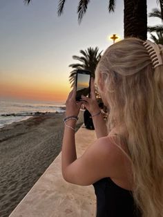 a woman taking a photo with her cell phone on the beach at sunset or dawn