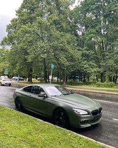 a green car is parked on the side of the road in front of some trees