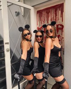 three women dressed up as mickey mouses in front of a door with blood on the wall