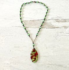 Vintage Czech Art Glass Pendant NecklaceA beautiful vintage to antique Art Deco Czech glass pendant necklace in a lovely shade of green.The pendant is a marquise green glass piece with a red foil iridescent pattern that looks like lava. It measures 1 3/4 inches tall, 7/8 inches wide, and 3/16 inches thick.The rosary chain comprises round green satin glass beads, each capped by a tiny metal filigree cap. The round beads are 1/4 of an inch.In very good condition with light wear consistent with age Murano Glass Necklaces, Czech Art, Art Deco 1920s, Red Foil, The Rosary, Jewelry Tags, Rosary Chain, Necklace Green, Glass Pendant Necklace