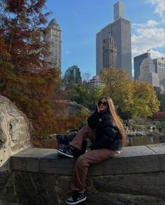 a woman sitting on top of a stone wall in front of a cityscape