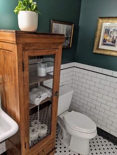 a bathroom with green walls and black and white tile flooring, a wooden cabinet over the toilet