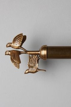 two brass birds are on the handle of a curtain rod, which is attached to a white wall