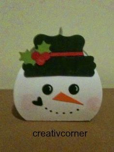 a white snowman with a black hat and holly on it's head sitting on a table