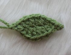 a green crocheted leaf laying on top of a white fur covered bed sheet