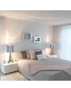 a white bedroom with pink and gray decor on the bed, nightstands and windows