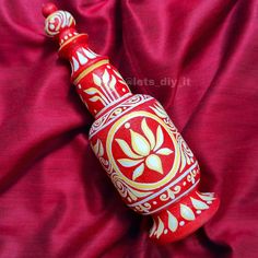 a red and white vase sitting on top of a pink cloth covered bed sheet with gold accents