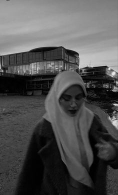 a woman wearing a headscarf is walking on the beach near some buildings and water