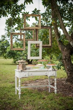 an old white table with pictures hanging from it's sides in front of a tree