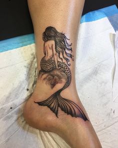 a woman's foot with a tattoo of a mermaid sitting on top of it