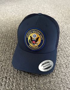 the navy blue hat has an eagle patch on it and is sitting on carpeted floor