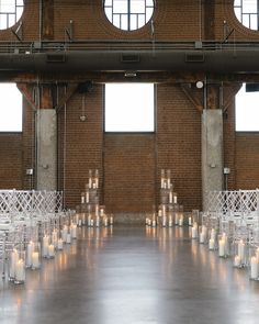 rows of white chairs with candles on them in front of a brick wall and windows