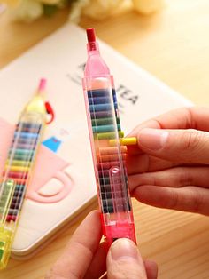 a person is holding some colorful crayons in their hand and they are next to a notebook