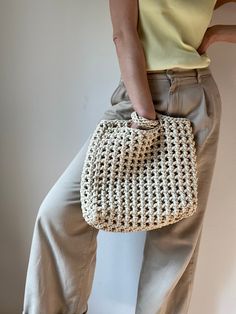 a woman is holding a crocheted purse in her right hand while standing against a wall