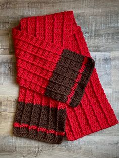 two red and brown knitted scarfs sitting on top of a wooden floor