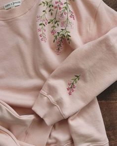 a baby's pink sweater with flowers on the front and bottom, sitting on a wooden surface