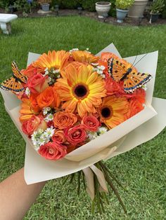 a bouquet of orange and yellow flowers with butterflies on them in the grass near a person's hand