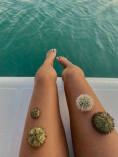 two people sitting on a boat in the water with their legs crossed and one person has dandelions on her leg