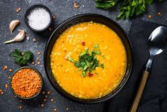 a bowl filled with soup next to two spoons and some other food on the table