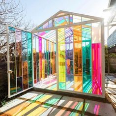 a colorful glass house sitting on top of a wooden floor next to a fence and trees