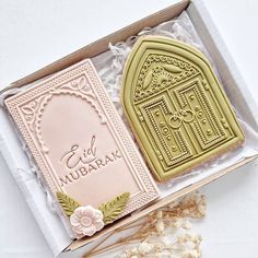 two decorated cookies in a box on top of a white table with lace and flowers