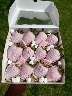 a box filled with lots of pink and white desserts on top of green grass