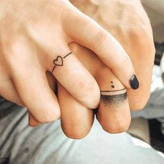 two people holding hands with tattoos on their fingers and one has a small heart tattoo