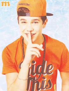 a young man in an orange shirt and hat posing for a photo with his finger on his lips