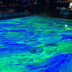 an indoor swimming pool with blue and green paint on the water, at night time