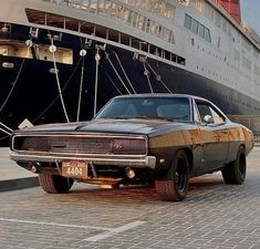 an old muscle car parked in front of a cruise ship